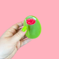 Hand holding a olive hair clip with a red center against a pink background
