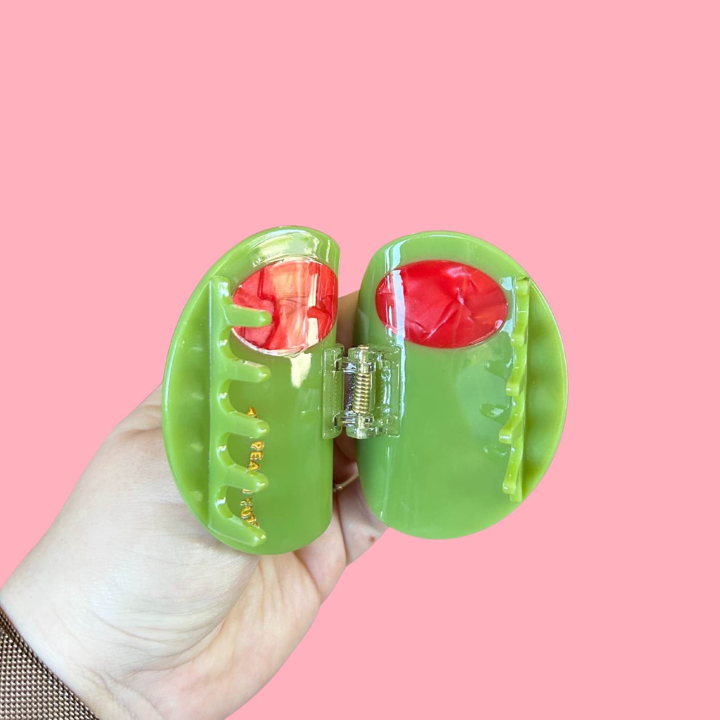 open green olive hair claw held against a pink background
