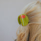 Person wearing a green olive hair clip in their hair on a plain background