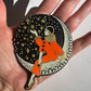 Circular decorative item with a person in an orange outfit and stars held in a hand.