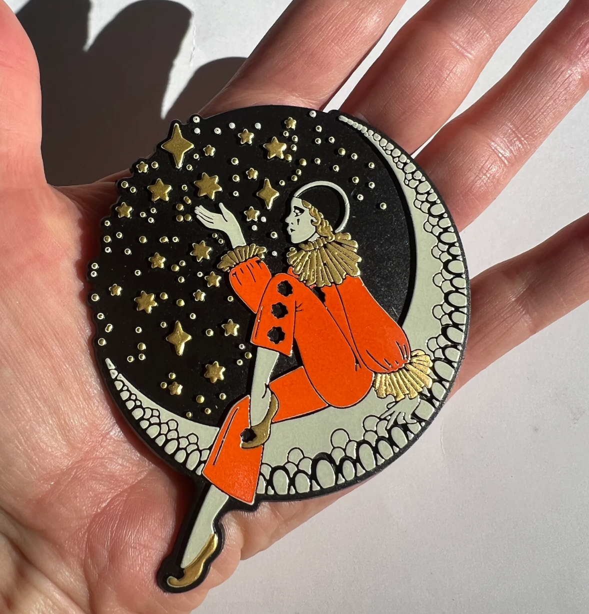 Circular decorative item with a person in an orange outfit and stars held in a hand.