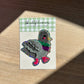 Shellflower glitter sticker on a checkered card with a wooden surface background