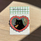 Sticker with a black cat eating pizza on a checkered background, brand 'Shellflower' visible