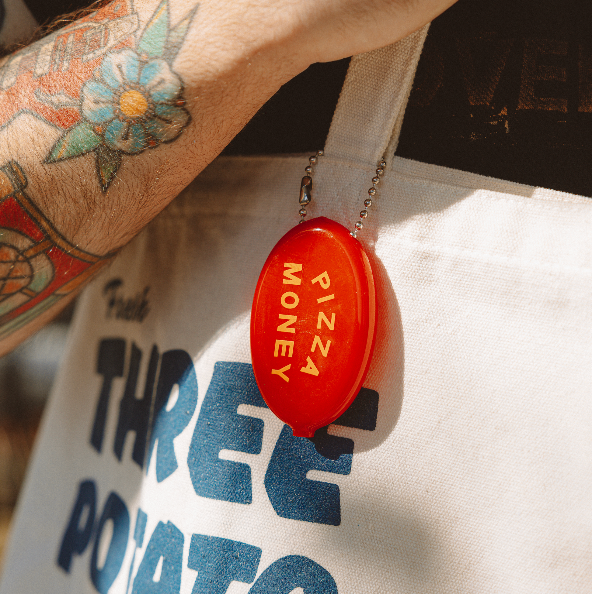 Red 'Pizza Money' container attached to a tote bag with text