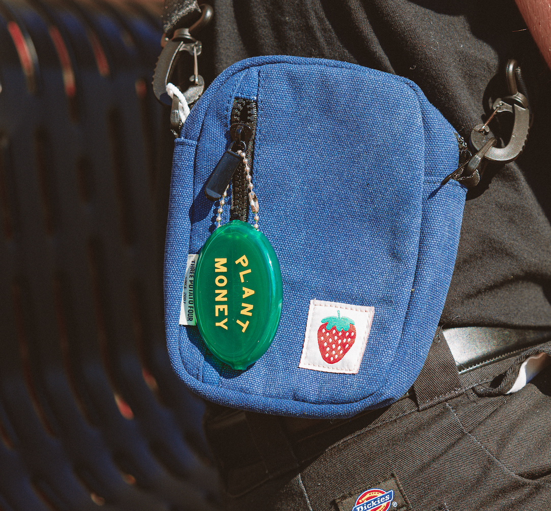 Blue pouch with a green 'Plant Money' tag attached to a person's bag.