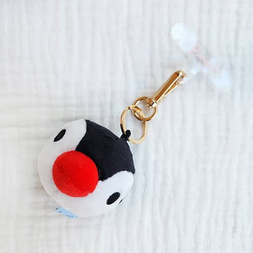Plush Pingu keychain with a red ball on a white textured background