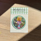 Sticker with a polly pocket character in a pink outfit on a wooden surface