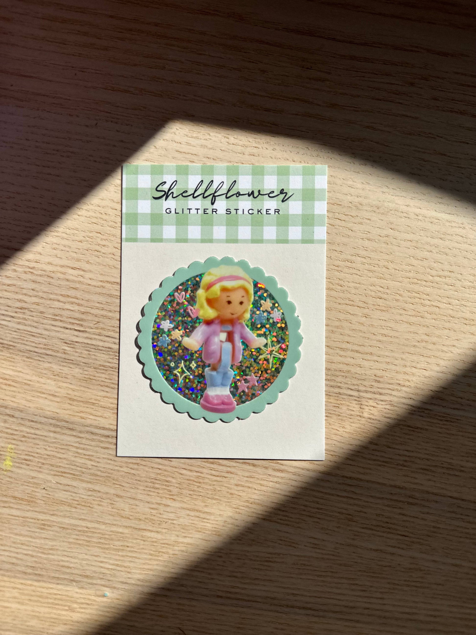 Sticker with a polly pocket character in a pink outfit on a wooden surface