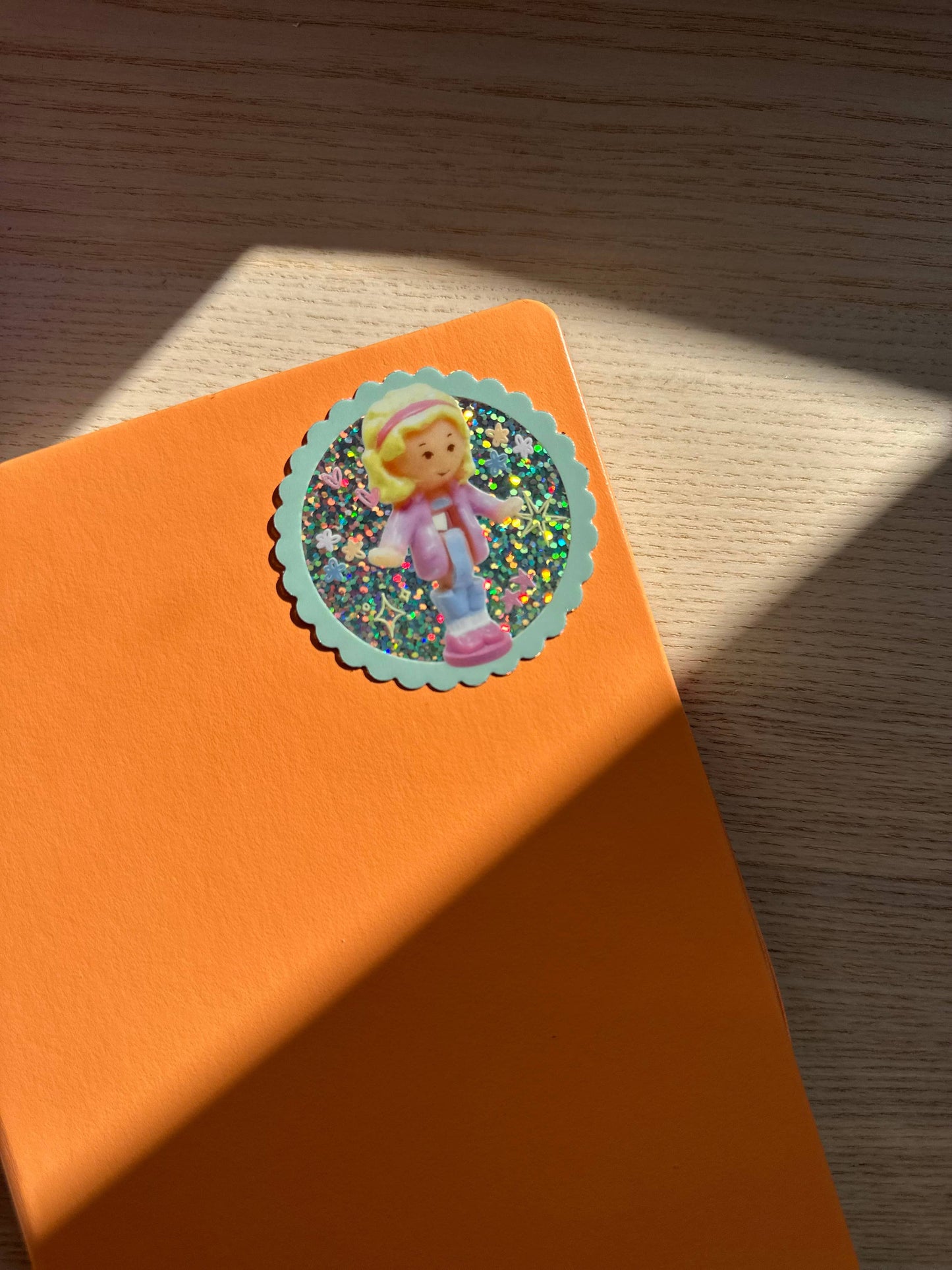 Orange notebook with a sticker of a polly pocket character on a wooden surface