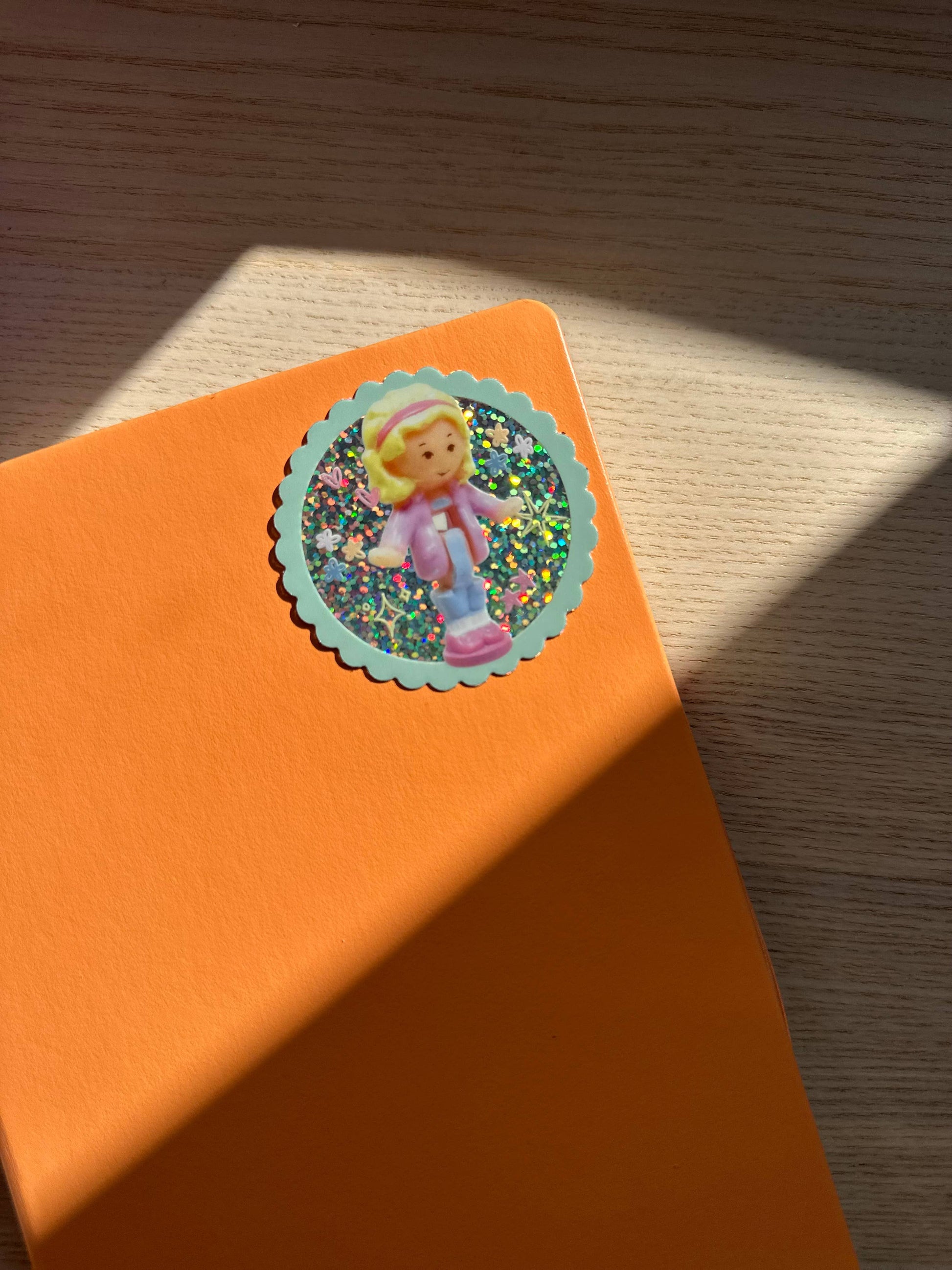 Orange notebook with a sticker of a polly pocket character on a wooden surface