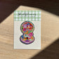 Shellflower glitter sticker on a wooden surface with a checkered border