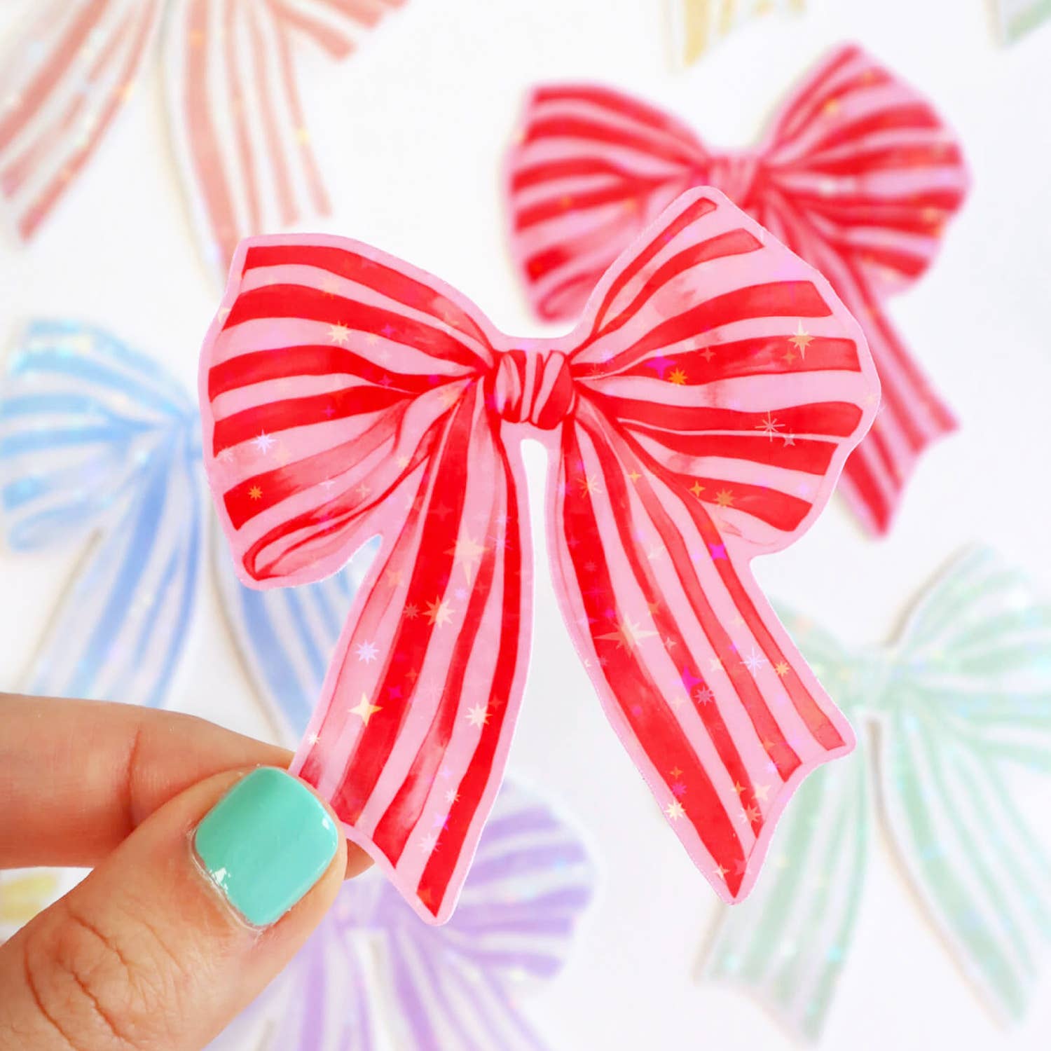 Red and pink striped bow held by a hand with teal nail polish against a colorful background.