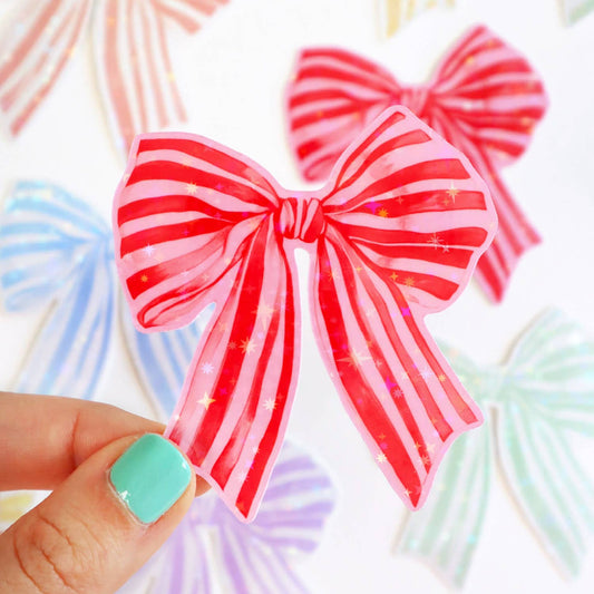 Red and pink striped bow held by a hand with teal nail polish against a colorful background.