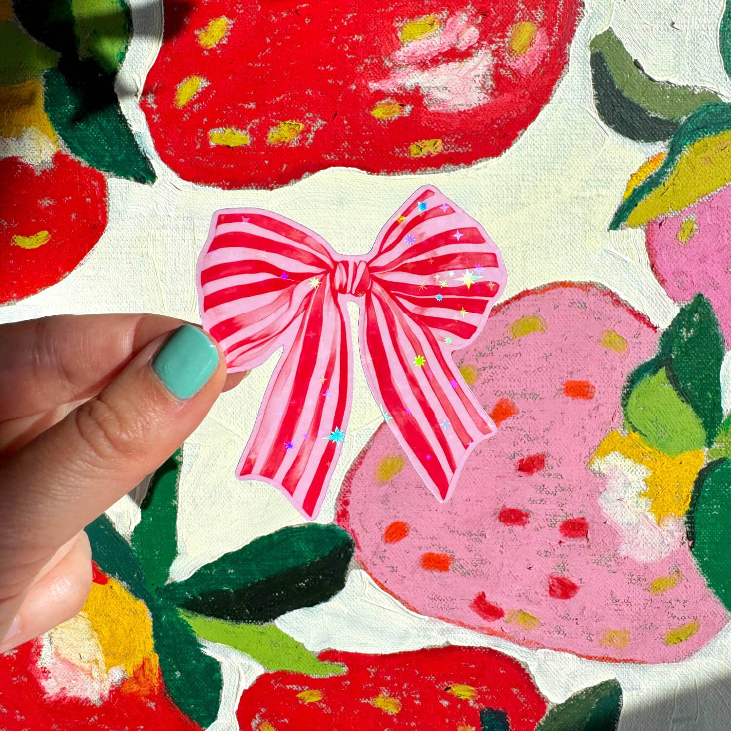 Hand holding a pink bow over a colorful fabric background with strawberries and flowers.