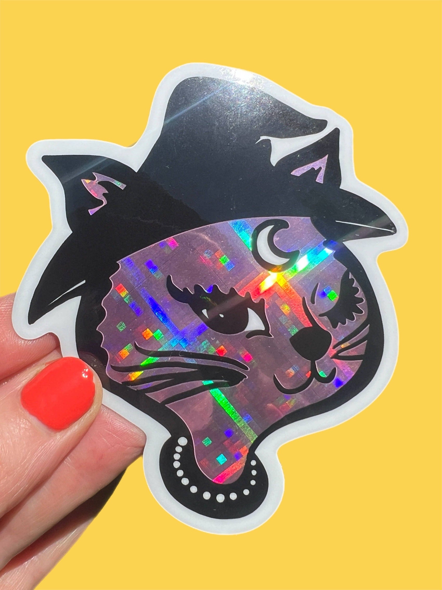 Holographic cat sticker held by a hand with red nail polish on a yellow background