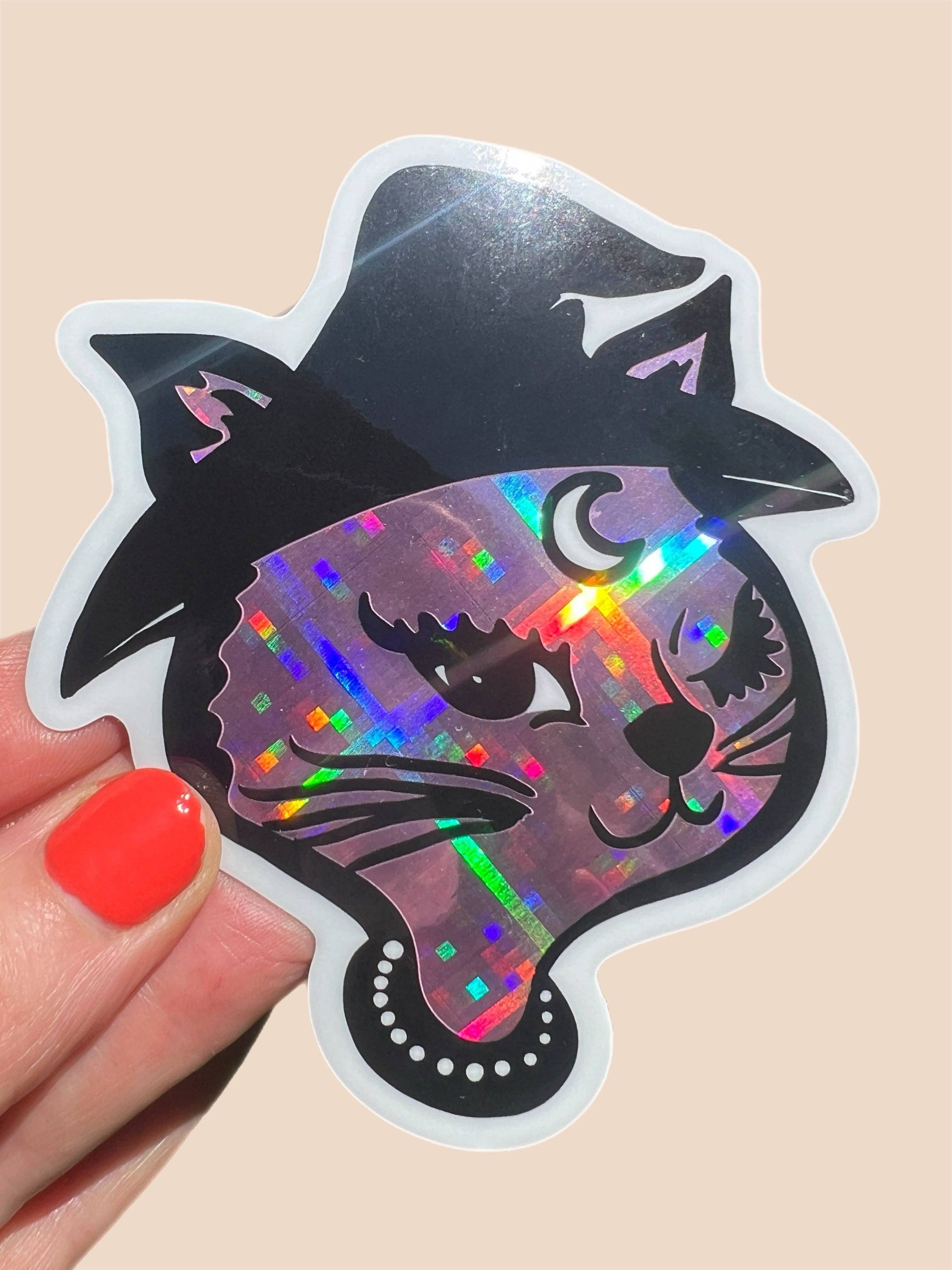 Holographic cat sticker held by a hand with red nail polish on a beige background