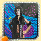 Sticker with a person in a glamorous outfit against a colorful background, held by a hand with orange nail polish.