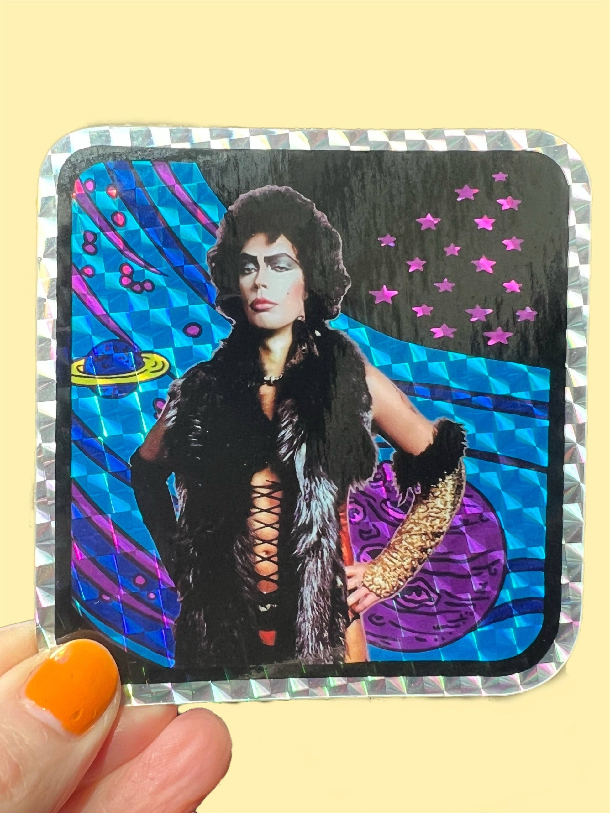 Sticker with a person in a glamorous outfit against a colorful background, held by a hand with orange nail polish.