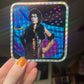 Holographic sticker held by a hand with orange nail polish.