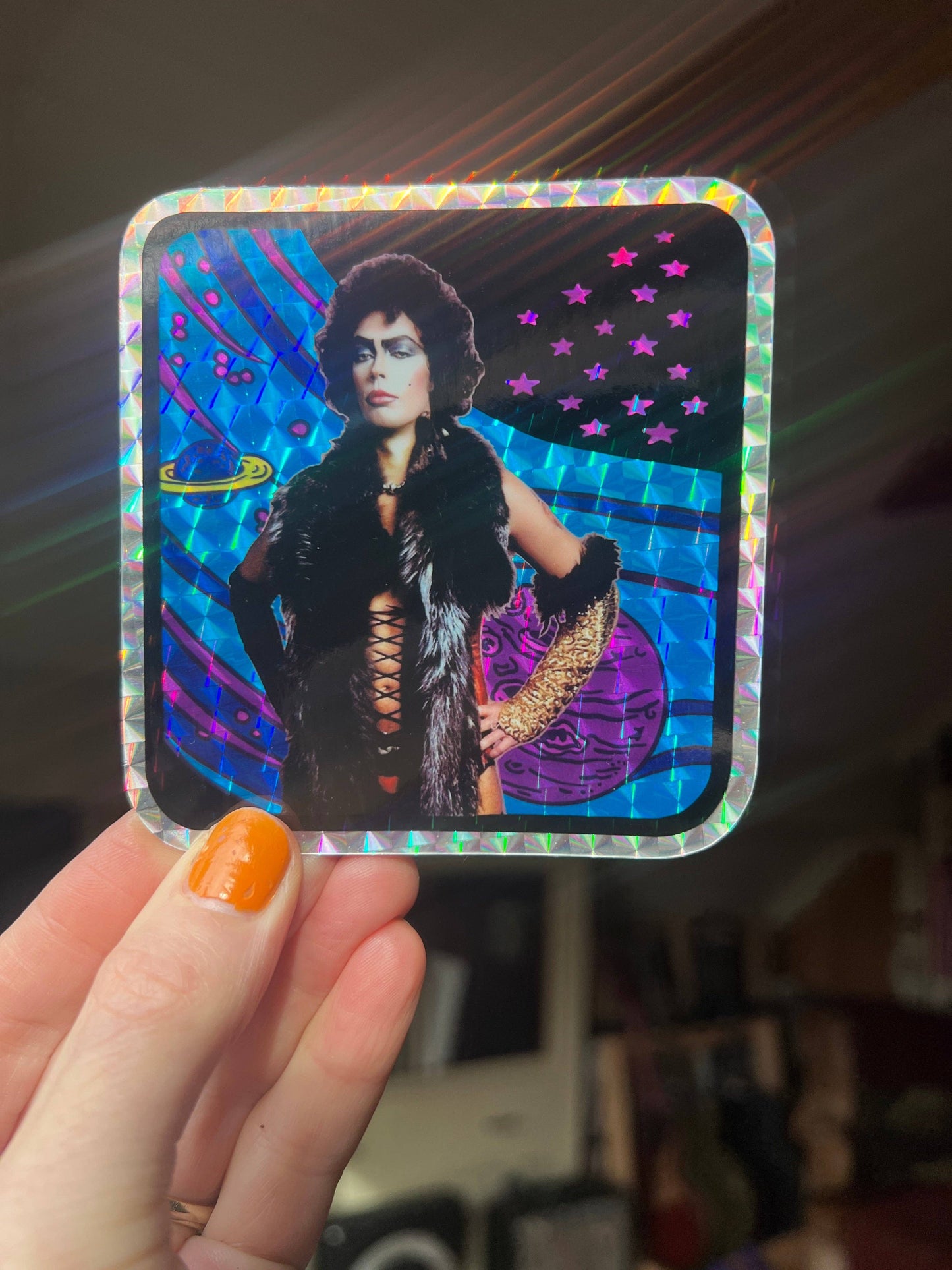 Holographic sticker held by a hand with orange nail polish.