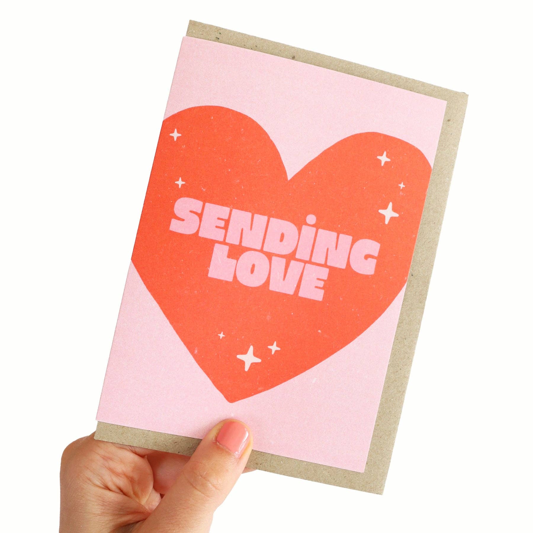 Card with a red heart and 'Sending Love' text on a pink background, held by a hand.