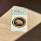 Hamster sticker on a Shellflower card with a checkered border, placed on a wooden surface.