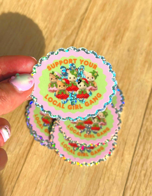 Colorful sticker with cartoon characters and text held by a hand on a wooden surface