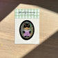Sticker with a shiba inu illustration on a green and white checkered card, placed on a wooden surface.