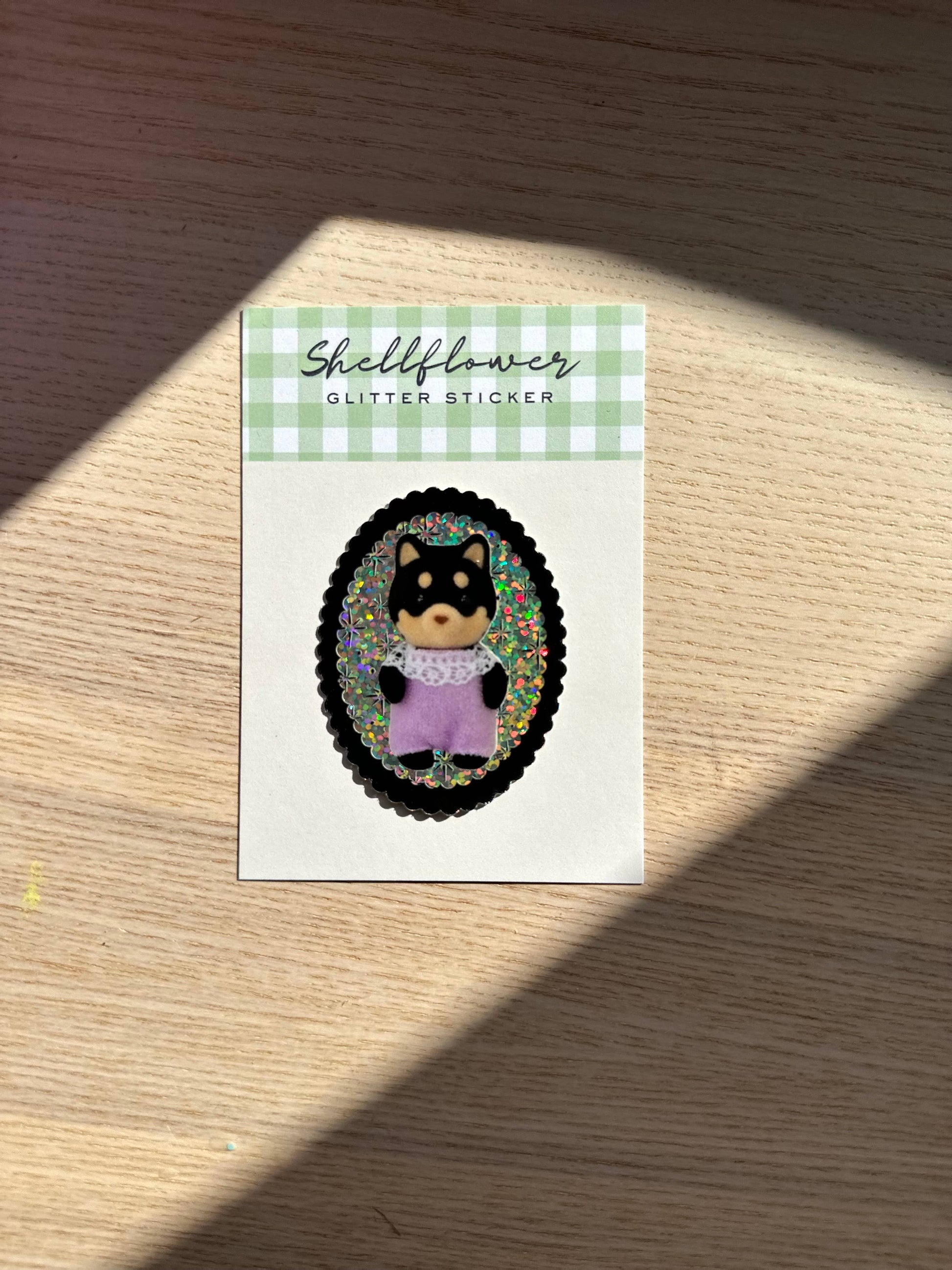 Sticker with a shiba inu illustration on a green and white checkered card, placed on a wooden surface.