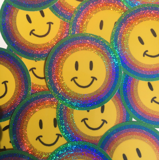 Stack of yellow smiley face stickers with multicolored glittery borders.