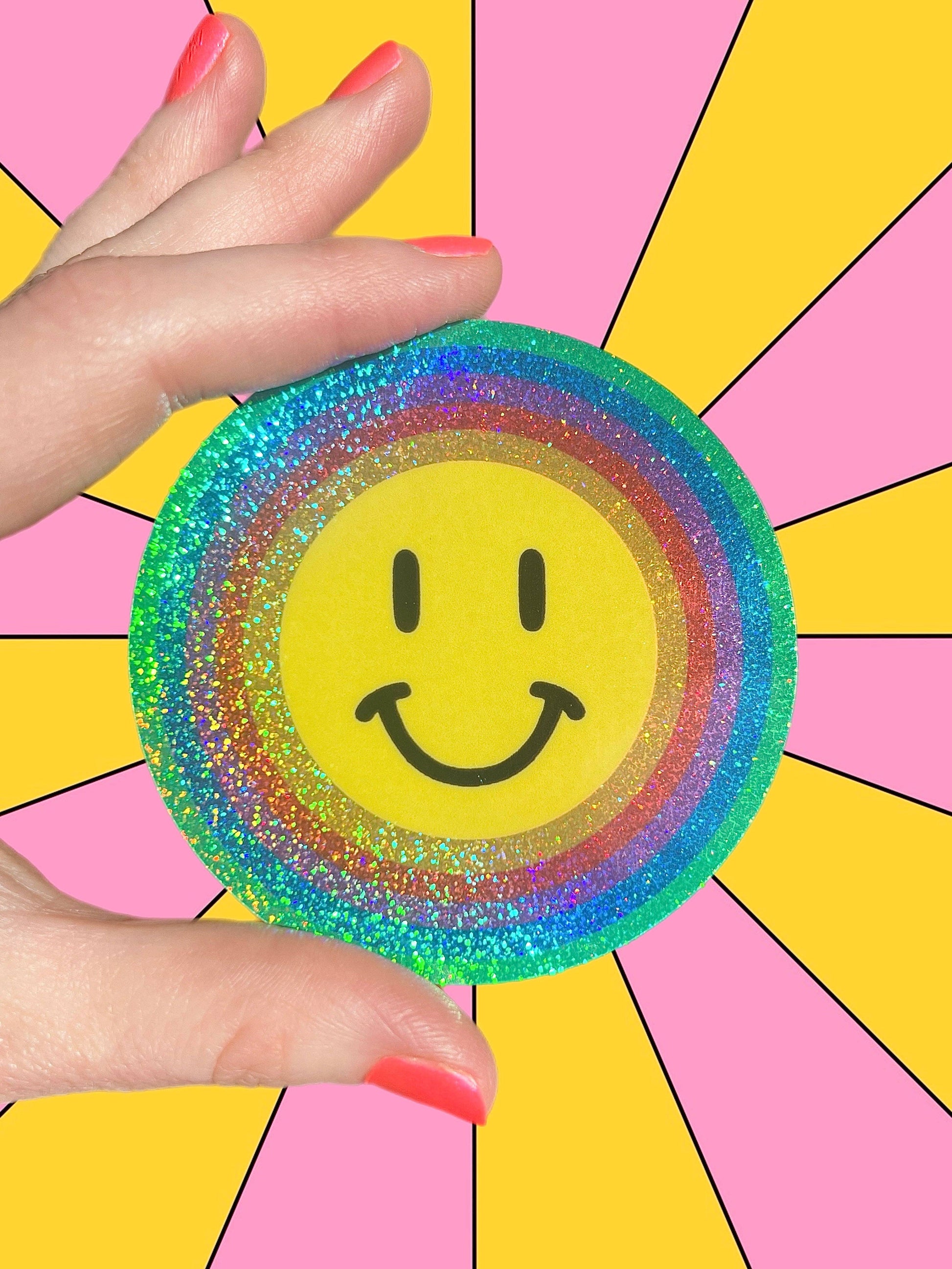 Hand holding a colorful smiley face sticker against a multicolored background