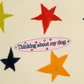 A close-up of a sticker that reads 'Thinking about my dog.' in blue script on a pink oval background, surrounded by small multicolored stars.
