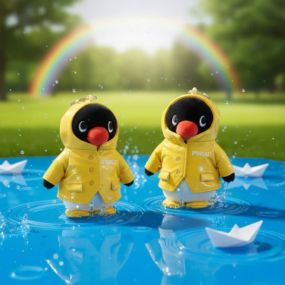 Two penguin figurines in yellow raincoats standing in water with paper boats and a rainbow in the background.