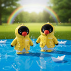 Two penguin figurines in yellow raincoats standing in water with paper boats and a rainbow in the background.