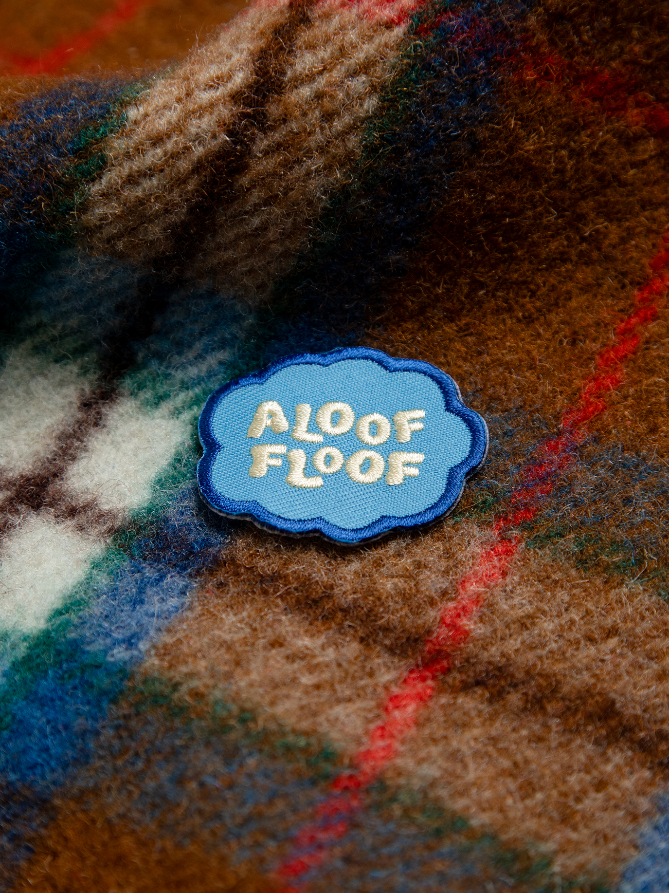 Patch with 'Aloof Floof' text on a plaid fabric background