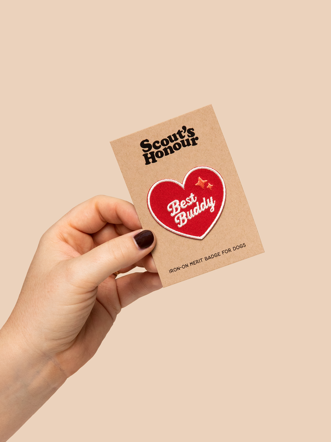 Hand holding a 'Scout's Honour' card with a heart-shaped badge on a beige background