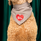 Dog wearing a checkered bandana with a heart-shaped 'Best Buddy' sign against a green curtain background
