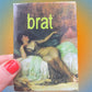 magnet with a classical painting cover and the word 'brat' in green text, held by a hand with red nail polish.