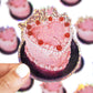 Pink cake-shaped sticker with cherries held by a hand against a blurred background
