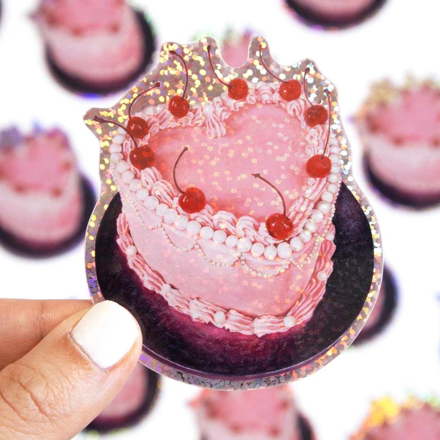 Pink cake-shaped sticker with cherries held by a hand against a blurred background