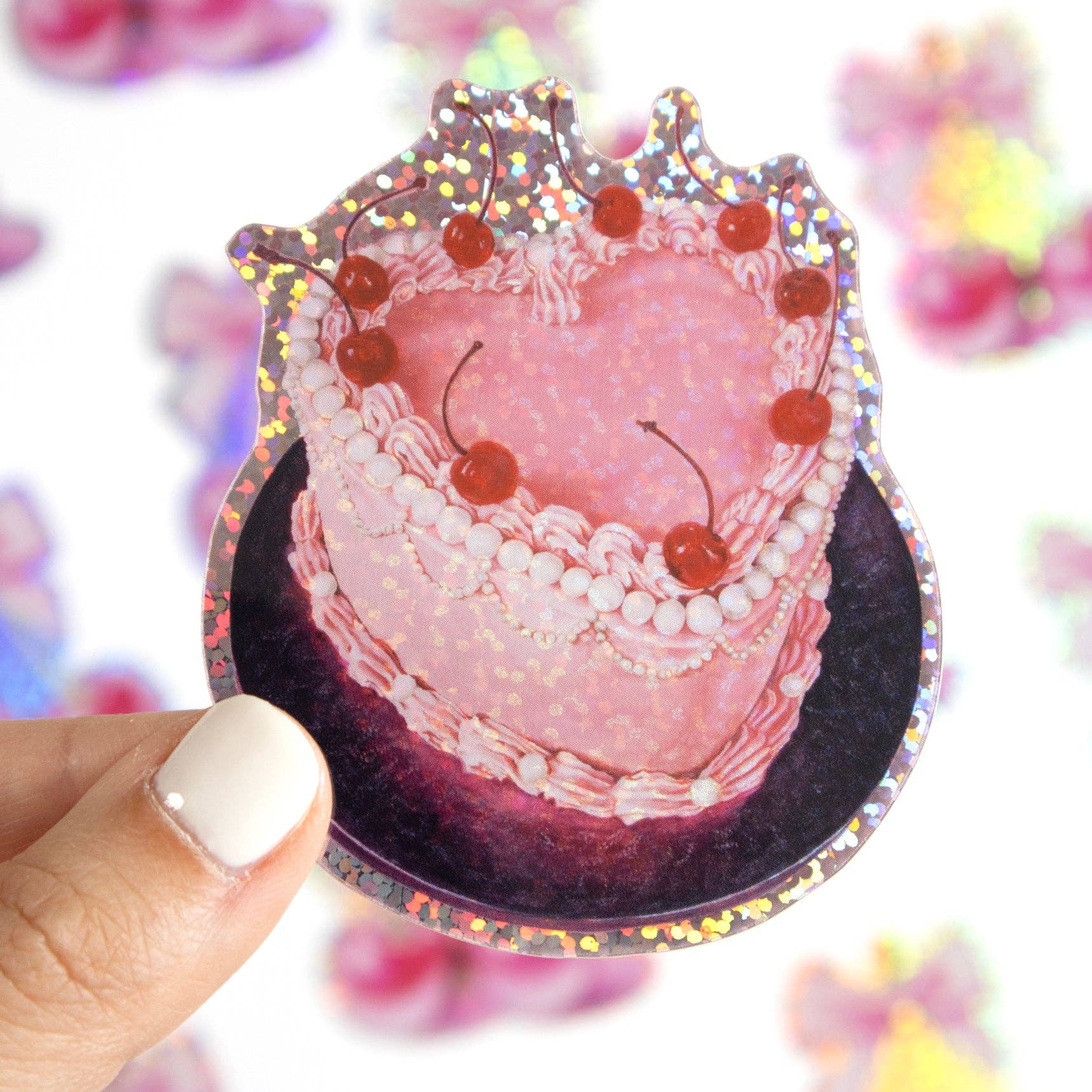 Heart-shaped cake with cherries and a crown on a reflective surface, held by a hand.
