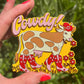 Cowdy! magnet held by a hand with red nail polish against a green leafy background