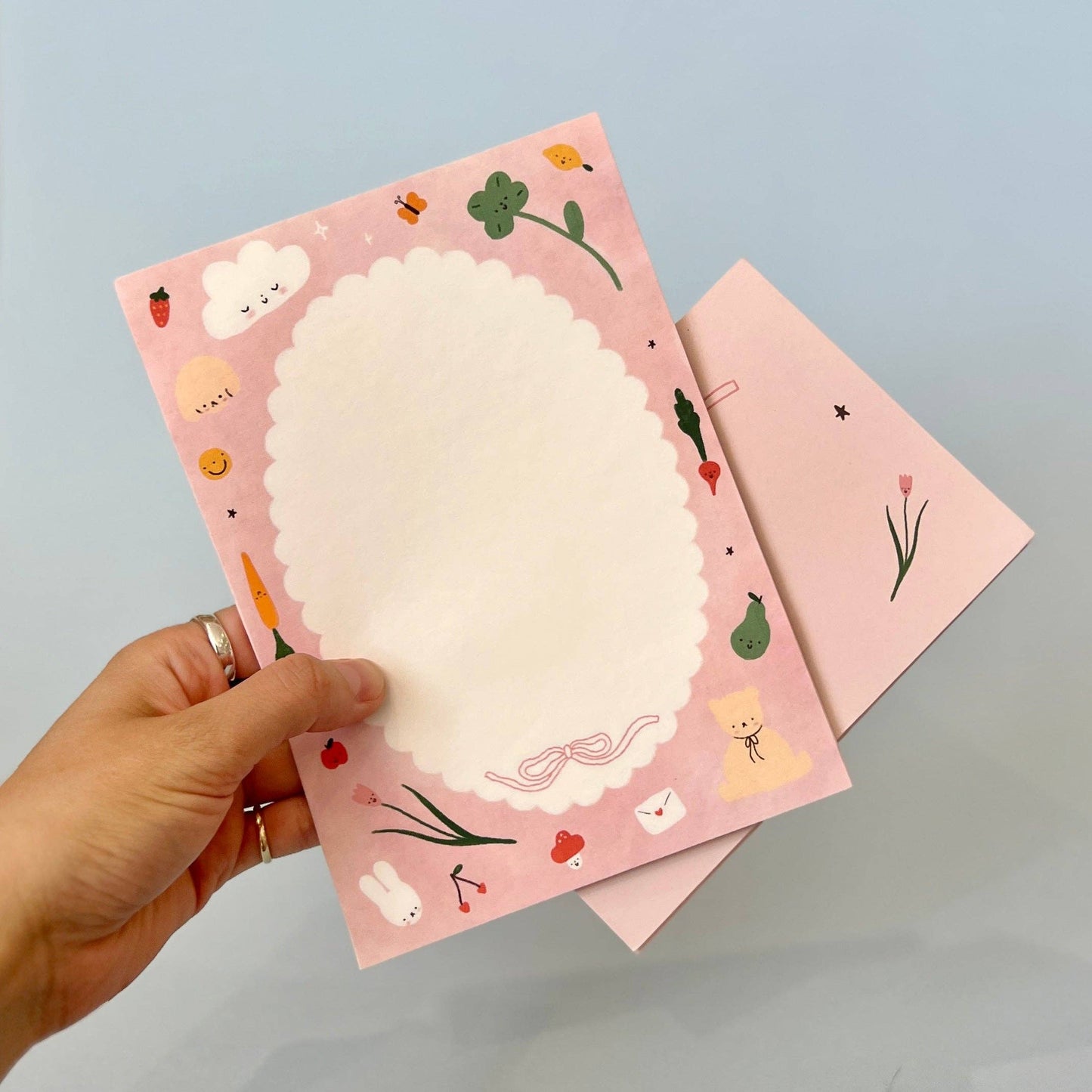 Hand holding a pink notebook with decorative cover against a light blue background