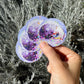 Hand holding two disco ball stickers against a natural background