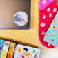 Colorful art supplies including a watercolor set and a disco ball on a wooden surface.