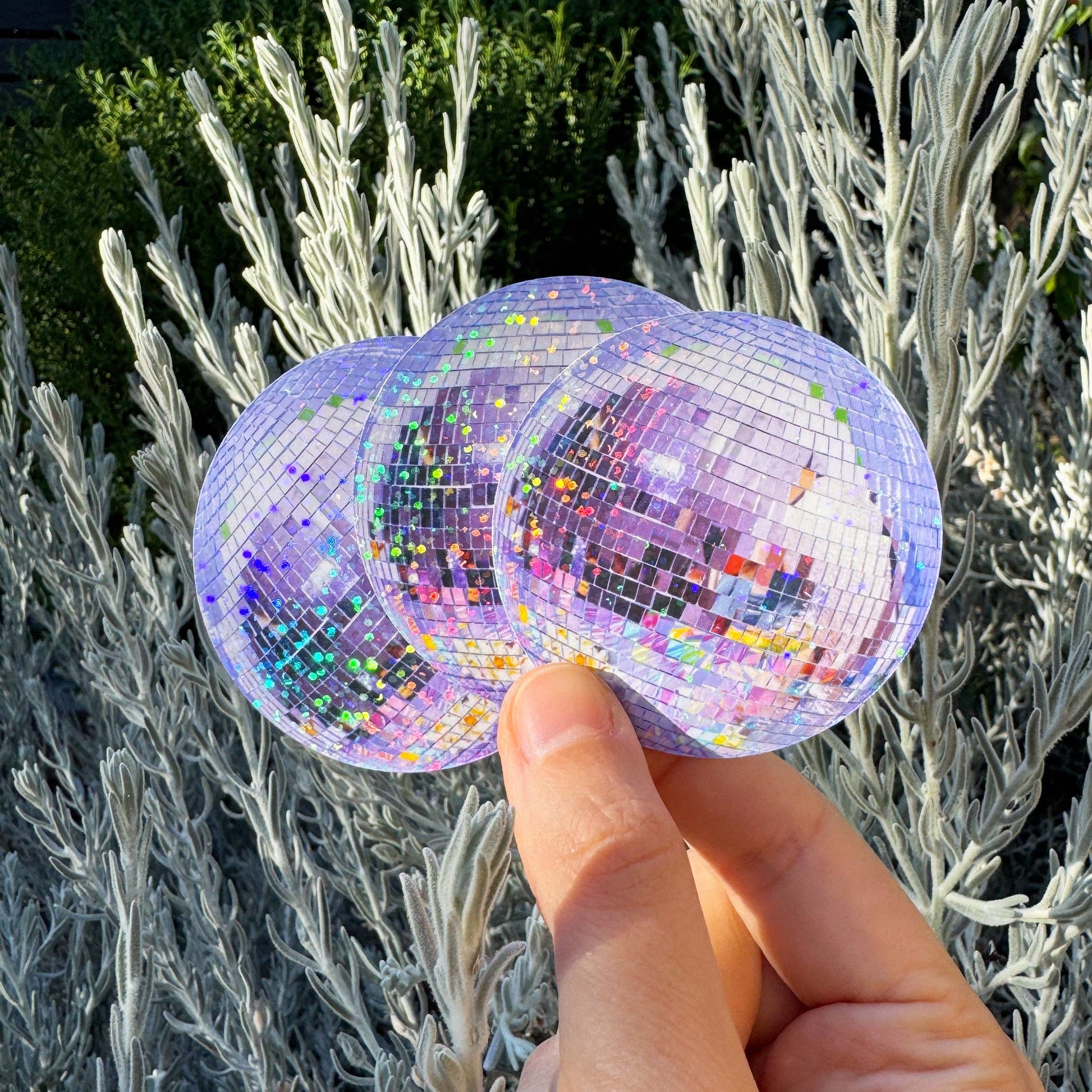 Hand holding disco ball stickers in front of a natural background