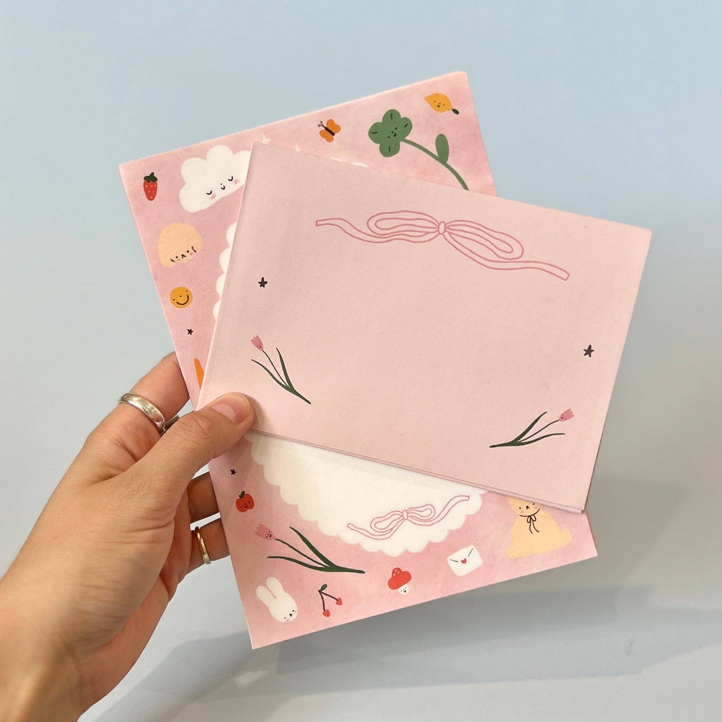 Hand holding two pink notebooks with cute illustrations on a light blue background