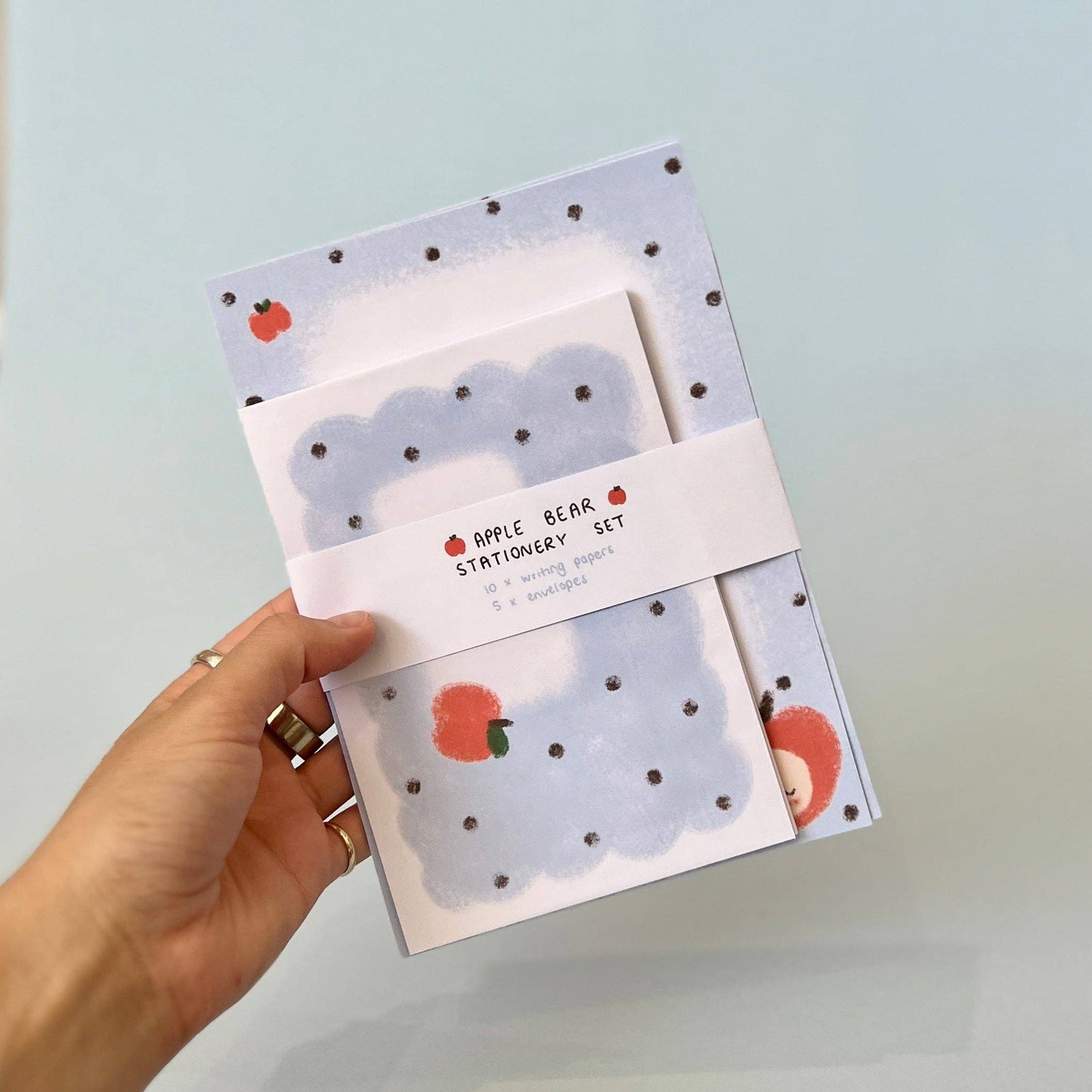 Hand holding a stationery set with bear and apple designs against a light blue background