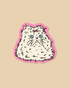 A die-cut sticker featuring a fluffy white cat with blue eyes and a pink bow, outlined in black and set against a pink border, displayed on a solid beige background.