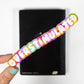 Colorful sticker with 'OVERSTIMULATED' text held by a hand against a black background